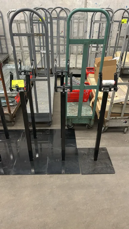 Metal roll bag dispenser stands. Features top-mounted wire roll bag dispensers and a black finish. Mounted on flat rectangular steel base plates. Roll