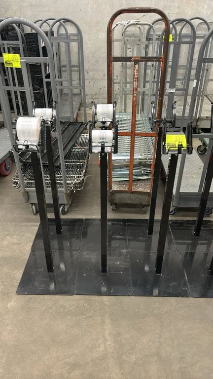 Metal produce bag dispenser stands. Features top wire roll bag holders and a black finish. Mounted on flat square metal base plates. Background items