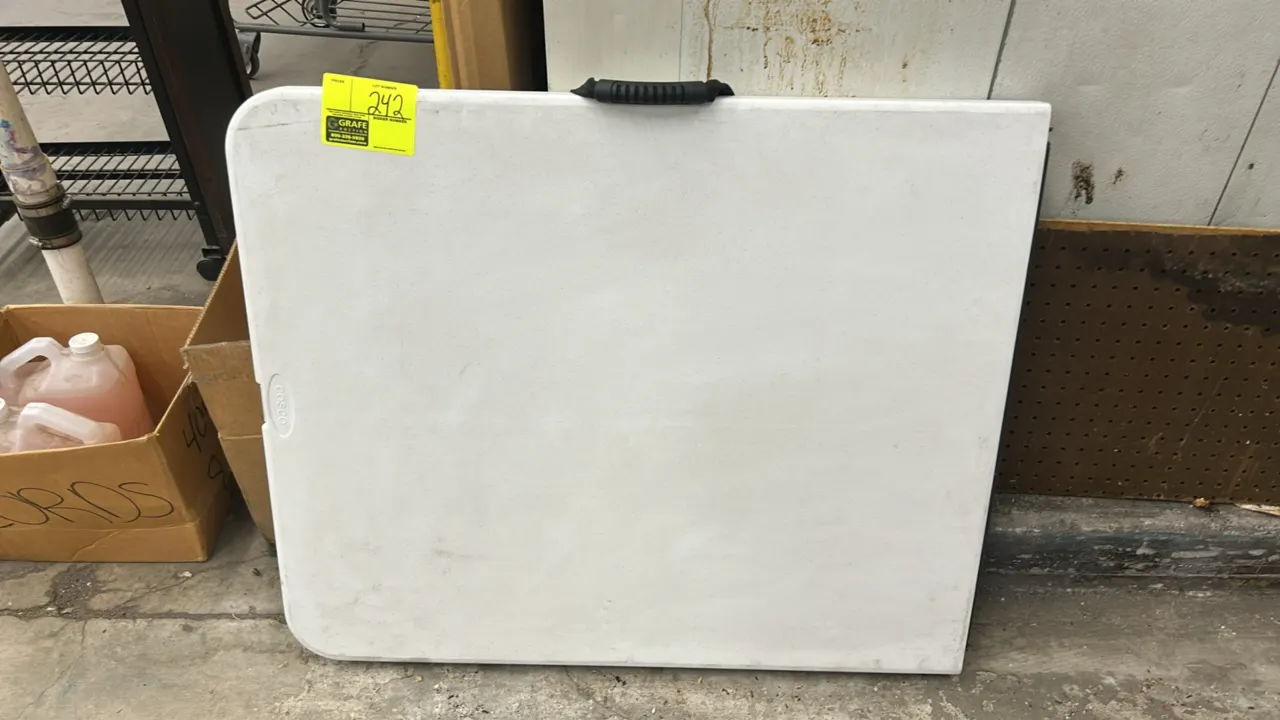 Cosco 6' folding table. Features a white molded polyethylene tabletop with a fold-in-half design and integrated carrying handle.
