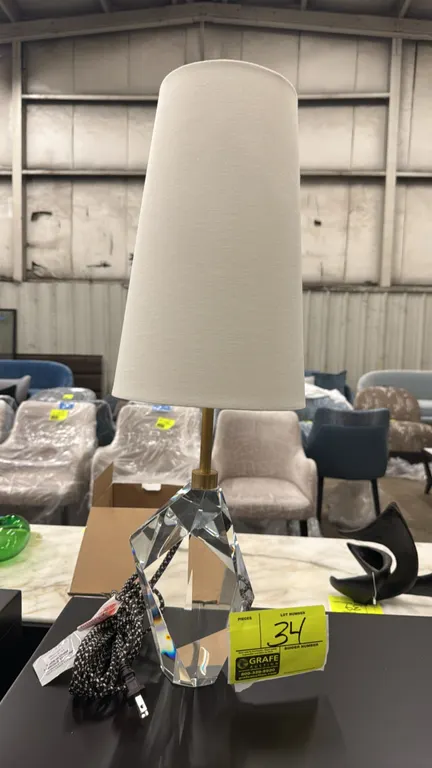 2022 KW3012CG-L table lamp. Features a faceted geometric glass base, brass-tone stem and finial, tall tapered fabric shade, and patterned braided cord