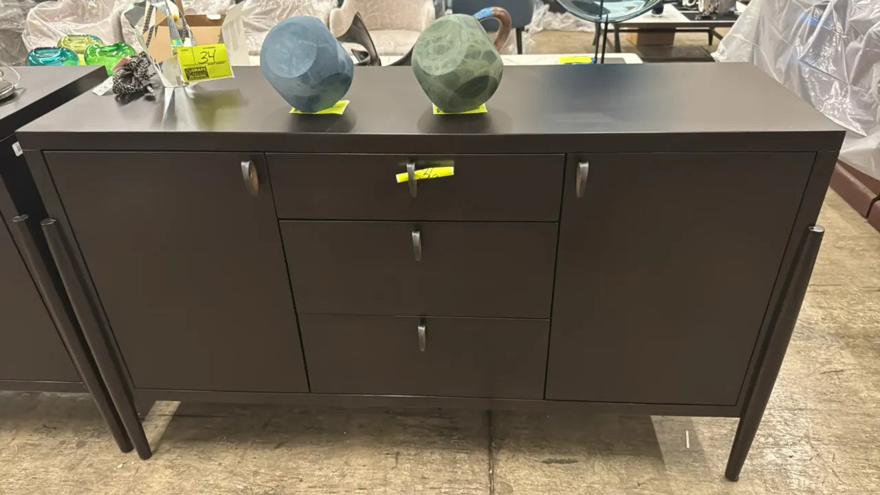 Dark brown sideboard credenza. Features 3 central self-closing drawers, 2 side storage cabinets with interior shelving, and bronze-tone pulls. Dimensi