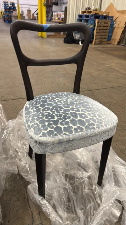 Porada Noemi dining side chair. Features a dark wood frame with an open curved backrest and tapered legs. Upholstered padded seat in a blue and cream