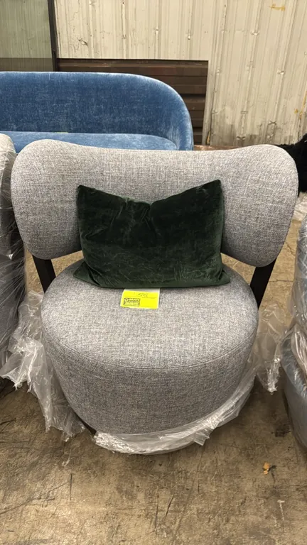Adriana Hoyos Rumba upholstered lounge chair. Features gray woven upholstery, black backrest support brackets, and includes a dark green accent pillow