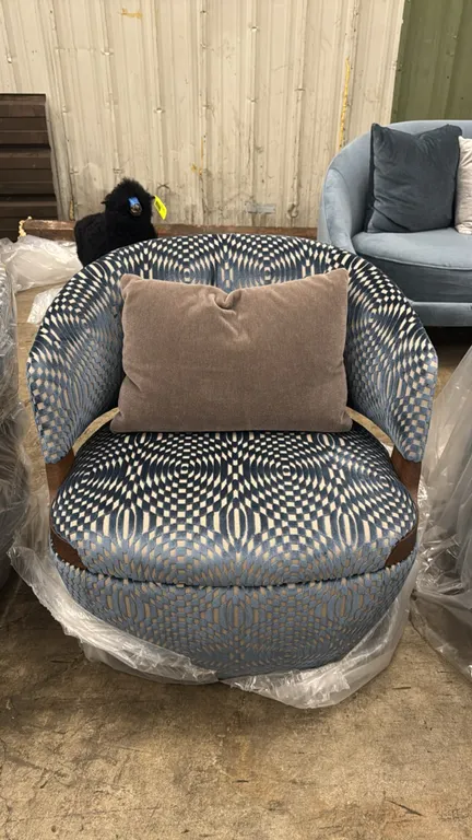 Potocco Velis armchair. Features blue mosaic patterned fabric upholstery, curved barrel back with exposed wood trim detail, and an included accent pil