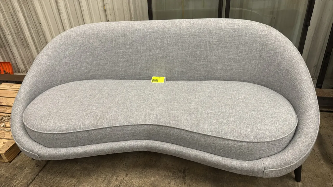 Custom upholstered sofa. Features light gray textured fabric upholstery, curved silhouette, and single fitted bench seat cushion. 84"L. Supported by d