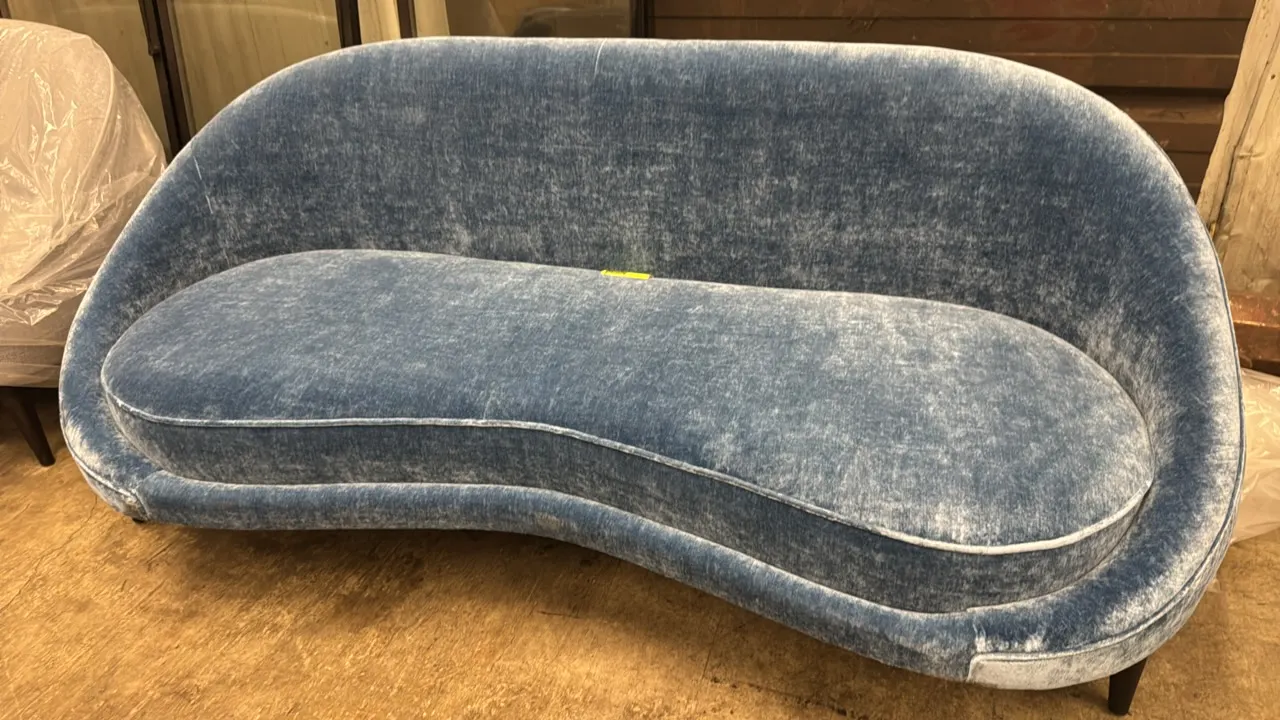 Custom upholstered plush sofa. Features blue plush fabric upholstery, curved kidney silhouette, single bench seat cushion with welt cord trim, and tap
