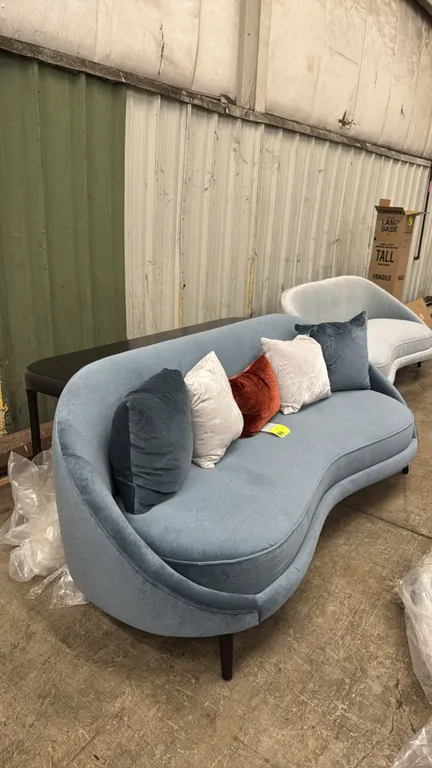 Custom curved sofa and sofa table set. Includes a 90"L curved blue upholstered sofa with tapered wood legs and (5) accent pillows, paired with a custo