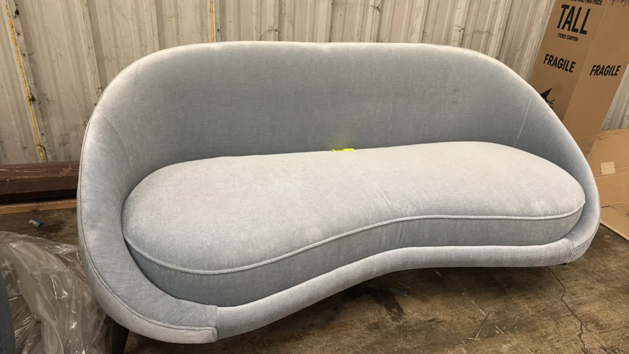 Custom upholstered sofa. Features a curved silhouette, plush light blue fabric upholstery, single removable seat cushion with welt cord trim, and tape