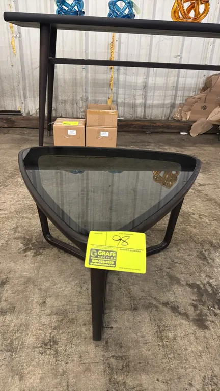 Wood side table with tinted glass top. Features a rounded triangular design with inset smoked glass and a sculpted dark wood three-point base. Dimensi