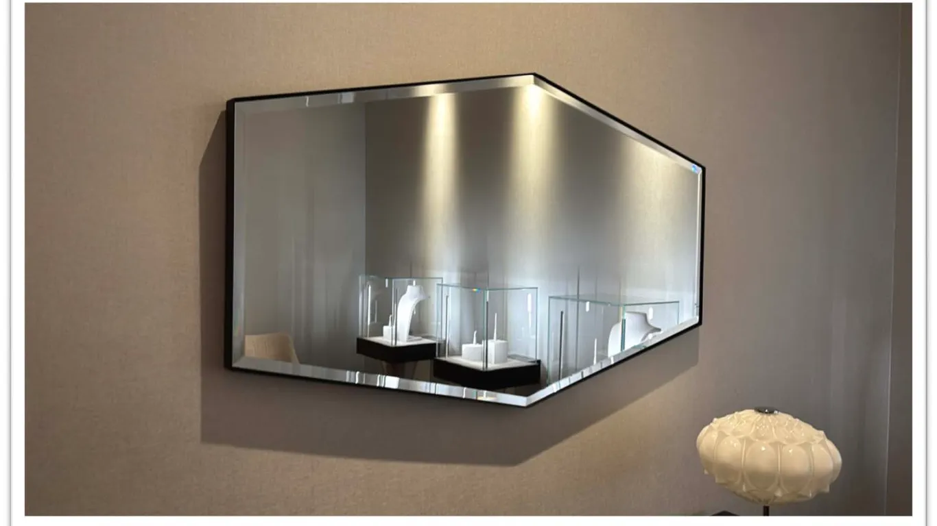 Metal-framed wall mirror. Features an elongated hexagonal geometric design, matte black metal frame, and beveled glass edge. Dimensions: 48" x 27".