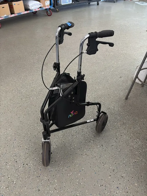 NOVA black three-wheel rollator walker with a black storage bag and hand brakes.