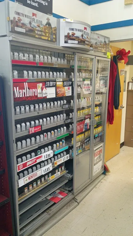 Metal merchandise display rack. Features wire grid backing, adjustable shelving with spring-loaded product pusher trays, price channels, overhead adve