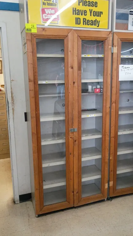 Display shelving units with glass doors. Features dual wood-framed glass hinged doors, multi-tier interior shelving, latch hasps, and upper signage he