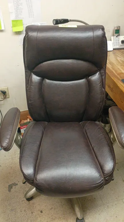 Serta executive computer chair. Features brown faux leather upholstery, contoured back with lumbar support, and padded armrests. Mounted on a 5-star s