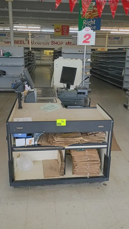 Single belt grocery check lane. Features a motorized conveyor belt, integrated scanner/scale cutout, bagging deck, and lower shelving storage compartm