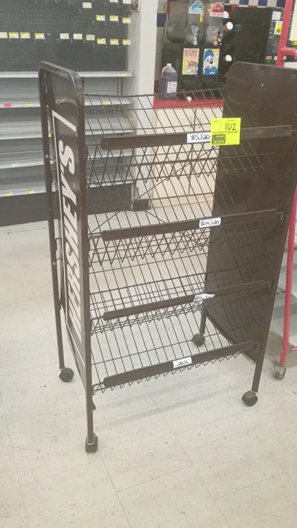 Hershey's 4-tier metal portable merchandise display rack. Features brown metal side panels with Hershey's branding and 4 angled wire shelves with fron