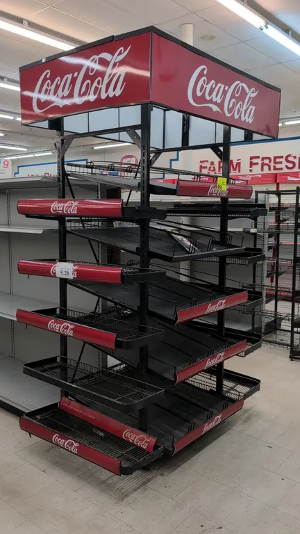 Coca-Cola metal merchandise display rack. Features Coca-Cola branded 4-sided header marquee, multi-tier wire and angled display shelves with red brand