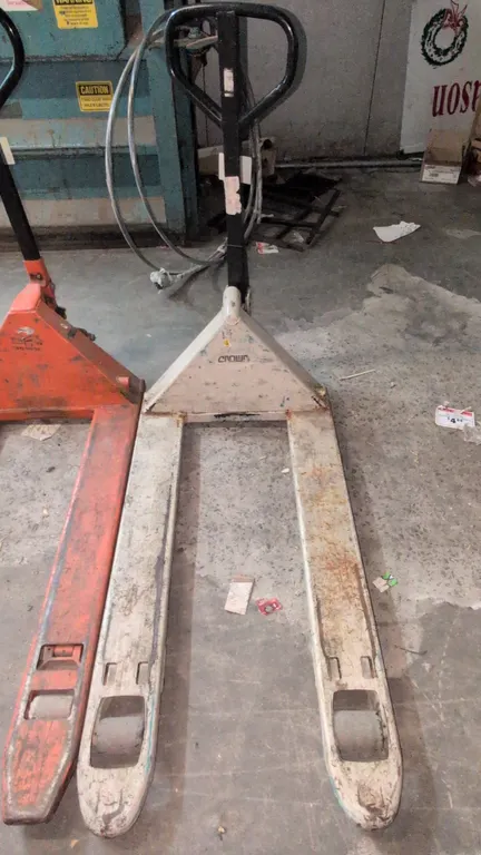 Crown PTH50 manual pallet jack. Features a 5,000 lb capacity, manual hydraulic pump handle with fingertip release lever, and dual front steer and fork