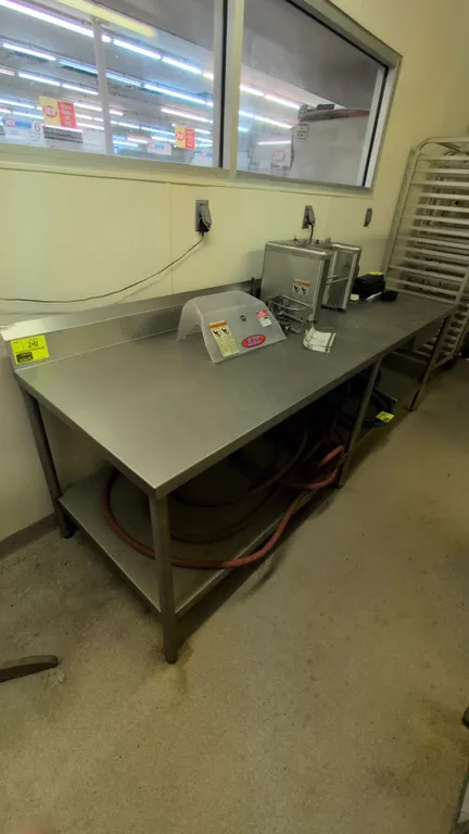 Stainless steel prep table. Features a rear backsplash, lower undershelf, and six tubular legs. Dimensions: 8'L. Contents not included.