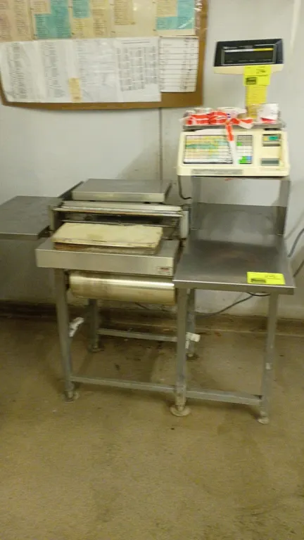 Heat Seal stainless steel heat seal wrapping station. Features an integrated film dispenser, hot plate seal pad, side prep shelf, and elevated scale s
