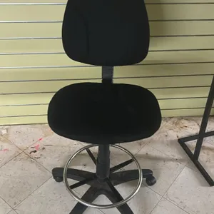 Upholstered armless drafting stool. Features black fabric cushioned seat and backrest, and an adjustable chrome-finish foot ring. Mounted on a 5-star 