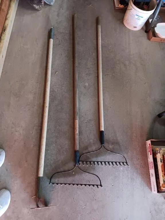 Metal rakes and hoe with wooden handles.