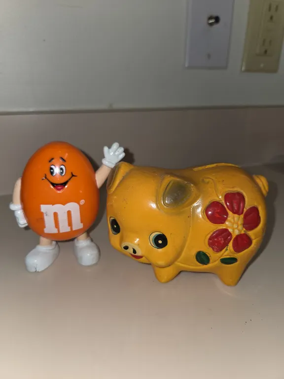 Vintage yellow ceramic/chalkwear piggy bank. Vintage 1991 orange M&M candy dispencer.