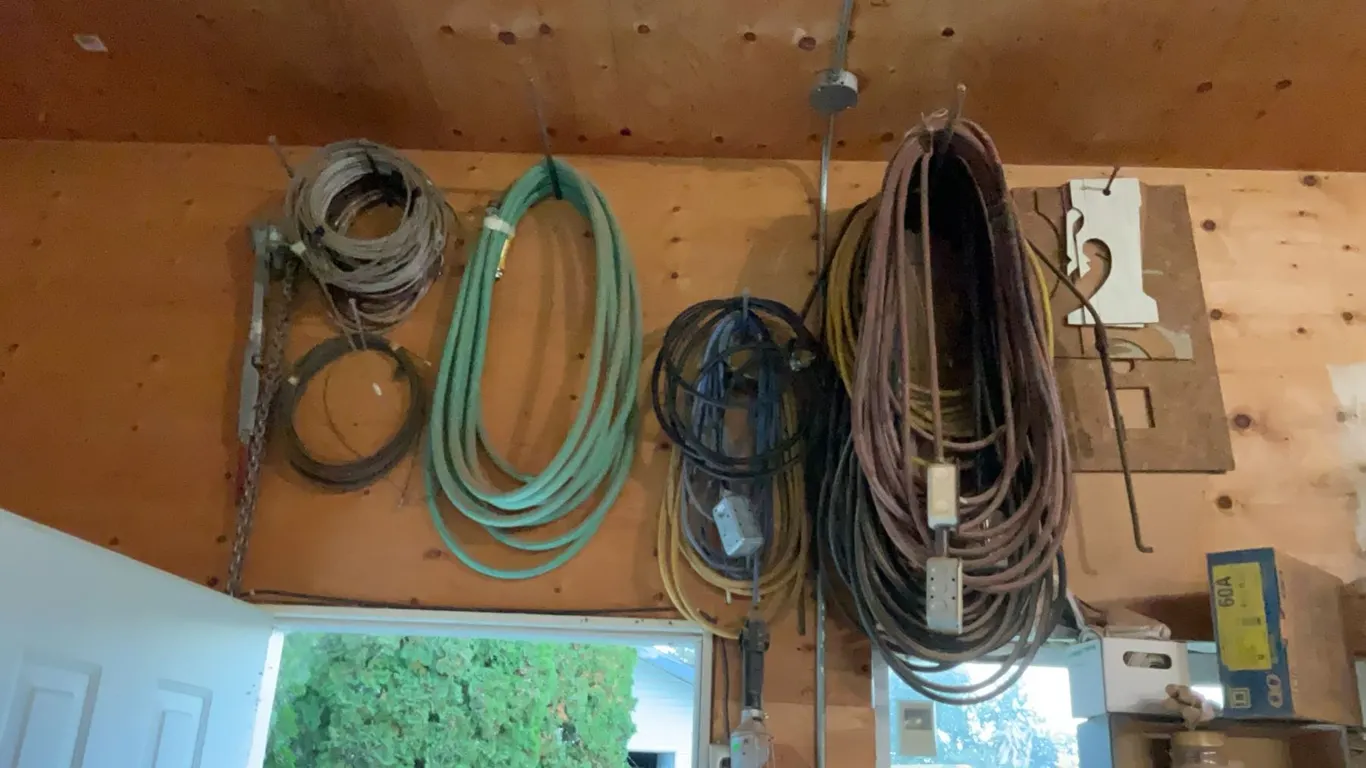 Extension Cords, Electrical Cables, Hose, and Chain Hanging From Wall
