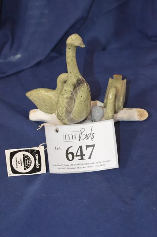 Three Swans Stand Guard Around A Nest Of Gray Eggs Lying On Swandown Filled Nest. On Whale Vertebrae