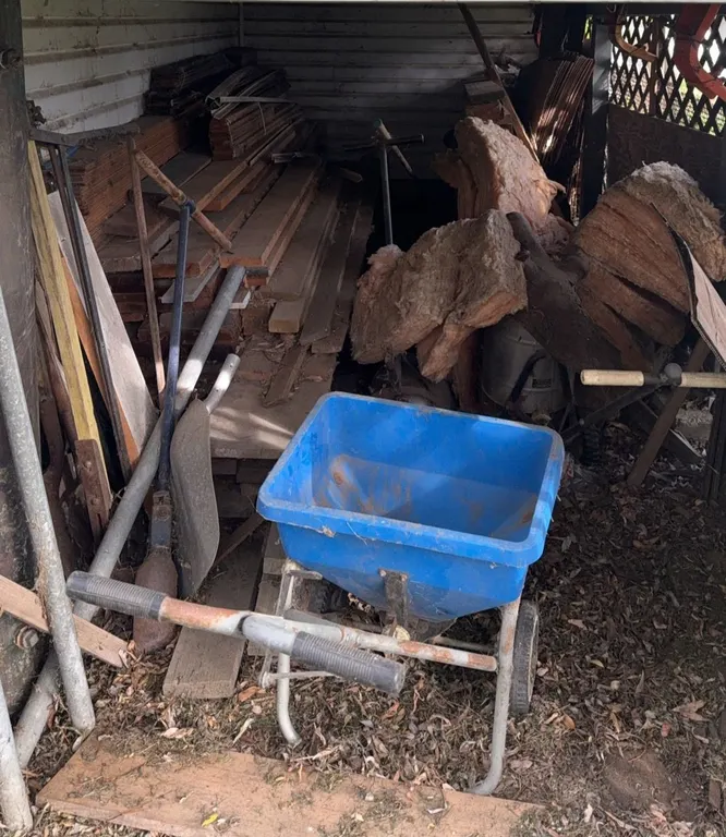 Building Materials and Tools Under Compound Including Wheelbarrow, Lumber, Pipes