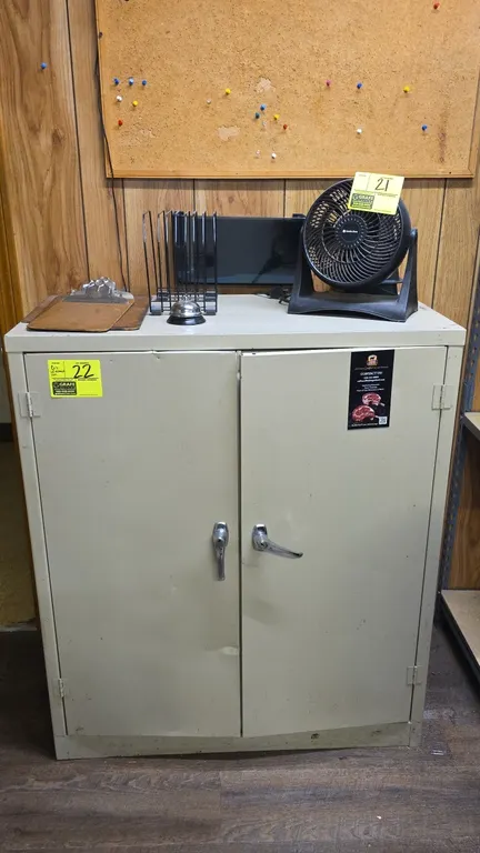 Metal double door storage cabinet. Features adjustable interior shelving and dual chrome latch handles. Includes assorted office supplies such as clip