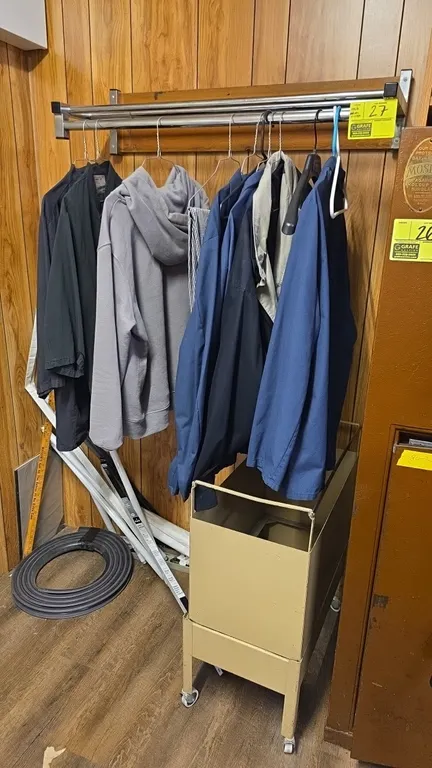 Metal wall-mounted clothes rack with clothes and metal cart. Clothes rack features a chrome tubular upper shelf and lower hanging rod on a wood mounti