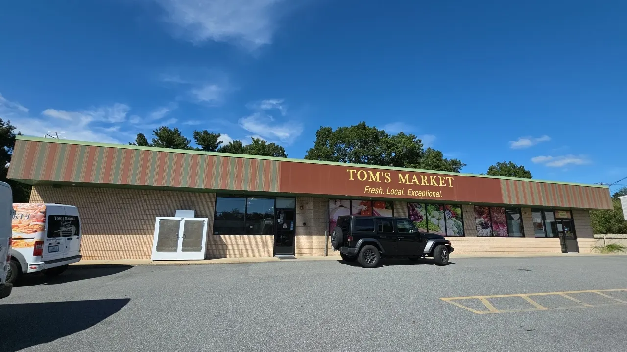 Multi-panel outdoor building fascia sign. Features center section reading "TOM'S MARKET / Fresh. Local. Exceptional." flanked by striped accent panels