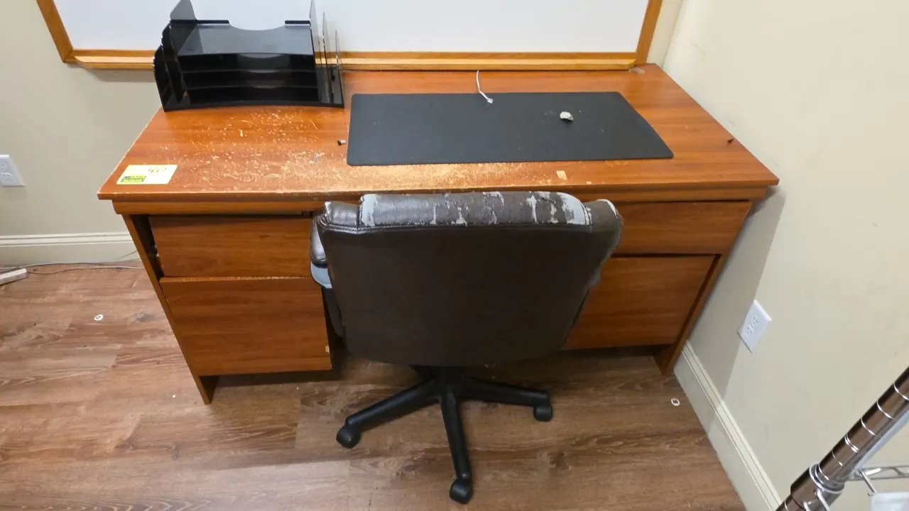 Laminate wood desk with office chair and desk accessories. Desk features a woodgrain laminate finish with storage drawers. Swivel chair is mounted on