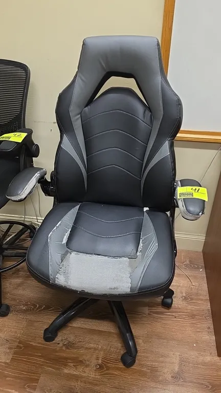 2019 SBG 52503 high-back gaming chair. Features black and gray faux leather upholstery, padded armrests, and pneumatic height adjustment. Mounted on a