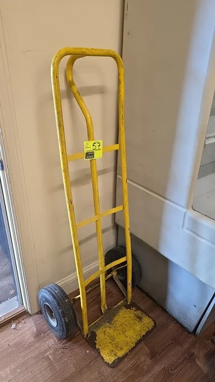 Two-wheel hand truck. Features yellow tubular metal frame, single loop handle, curved center brace, flat toe plate, and two pneumatic tires. Note: Ple