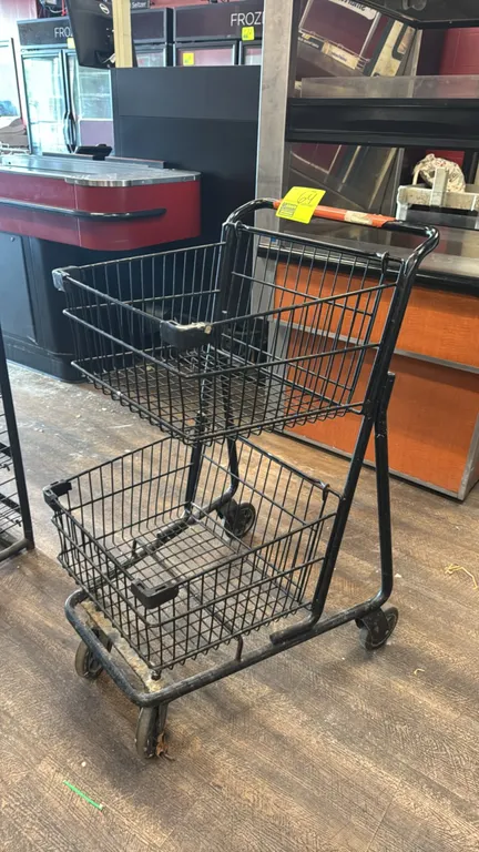 Metal two-basket shopping cart. Features black wire construction, two-tier basket design, and push handle. Mounted on casters.