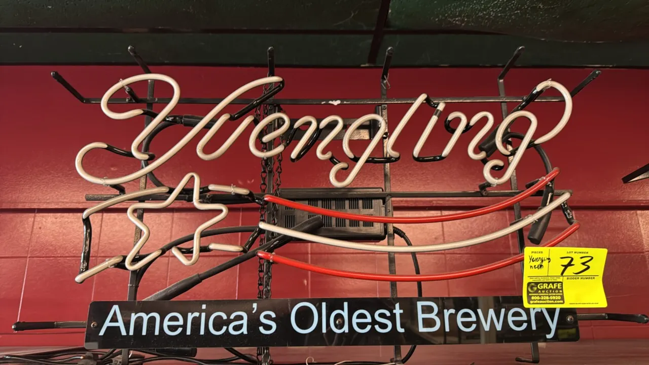 Yuengling neon beer sign. Features neon script lettering, star and stripe graphic, and lower panel reading "America's Oldest Brewery". Mounted on a bl