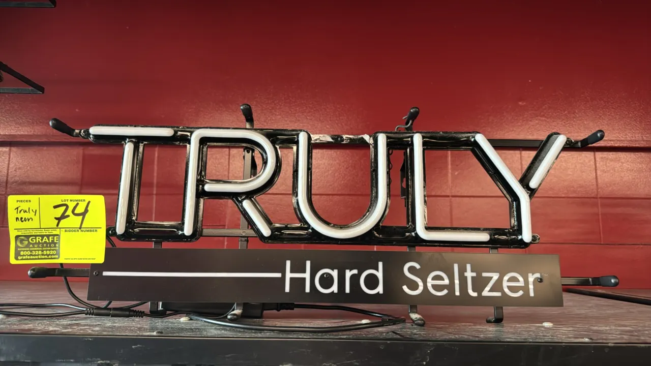 Truly Hard Seltzer neon advertising sign. Features white illuminated lettering and a lower 'Hard Seltzer' panel. 25" x 9". Mounted on a black metal fr