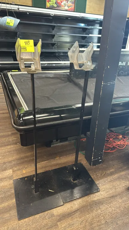 Metal produce bag stands. Features clear plastic roll bag dispensers mounted on metal uprights with flat rectangular base plates for freestanding plac