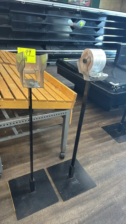 Metal produce roll bag dispenser stands. Features plastic roll dispenser holders mounted on black metal upright posts with flat base plates. Display t