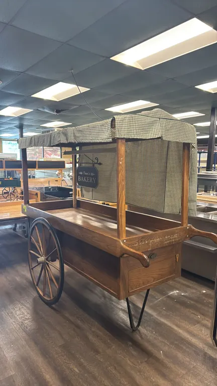 Wood wagon merchandiser display cart. Features fabric canopy cover, integrated overhead display light, hanging "Tom's Bakery" sign, enclosed lower sto