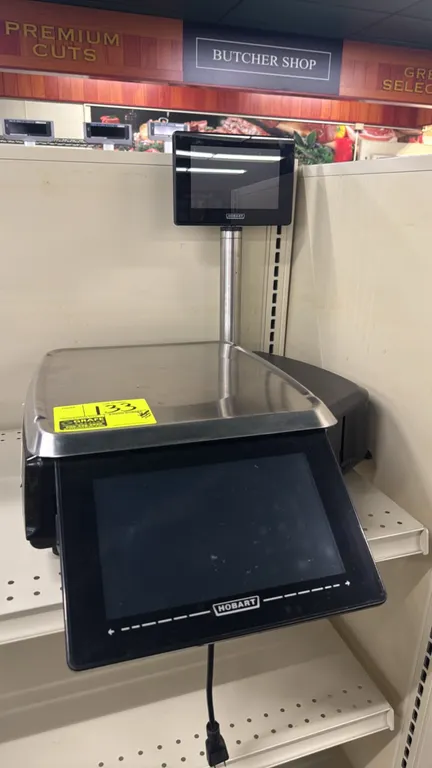 Hobart HTi electronic scale. Features touchscreen operator display, 9" customer display screen, integrated label printer, and stainless steel weigh pl