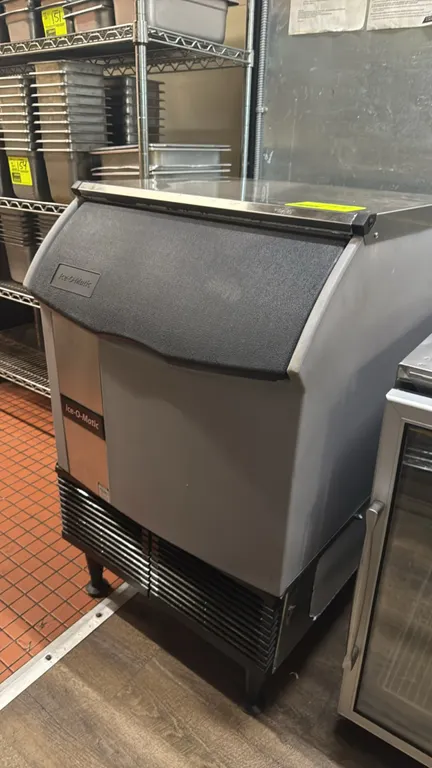 Ice-O-Matic ICEU220HA5 self-contained ice machine with built-in storage bin. Features a stainless steel top, front lift-up access door, and front vent