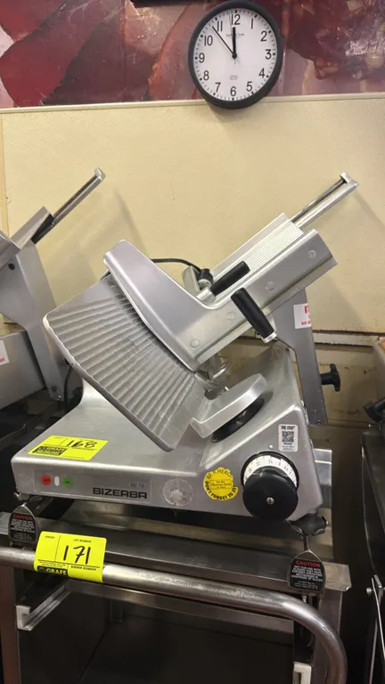 Bizerba SE 12 deli slicer. Features stainless steel and aluminum construction, gravity-feed product carriage with weighted pusher, and adjustable slic