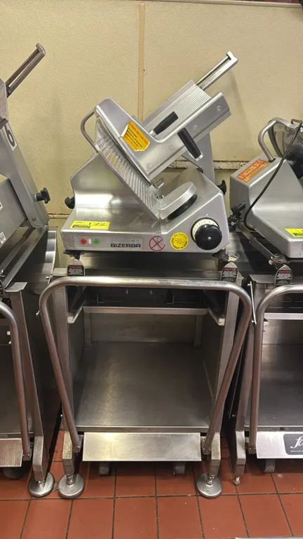 Bizerba SE 12 deli slicer with Deli Buddy stainless steel mobile stand. Slicer features gravity feed carriage, adjustable thickness control dial, and