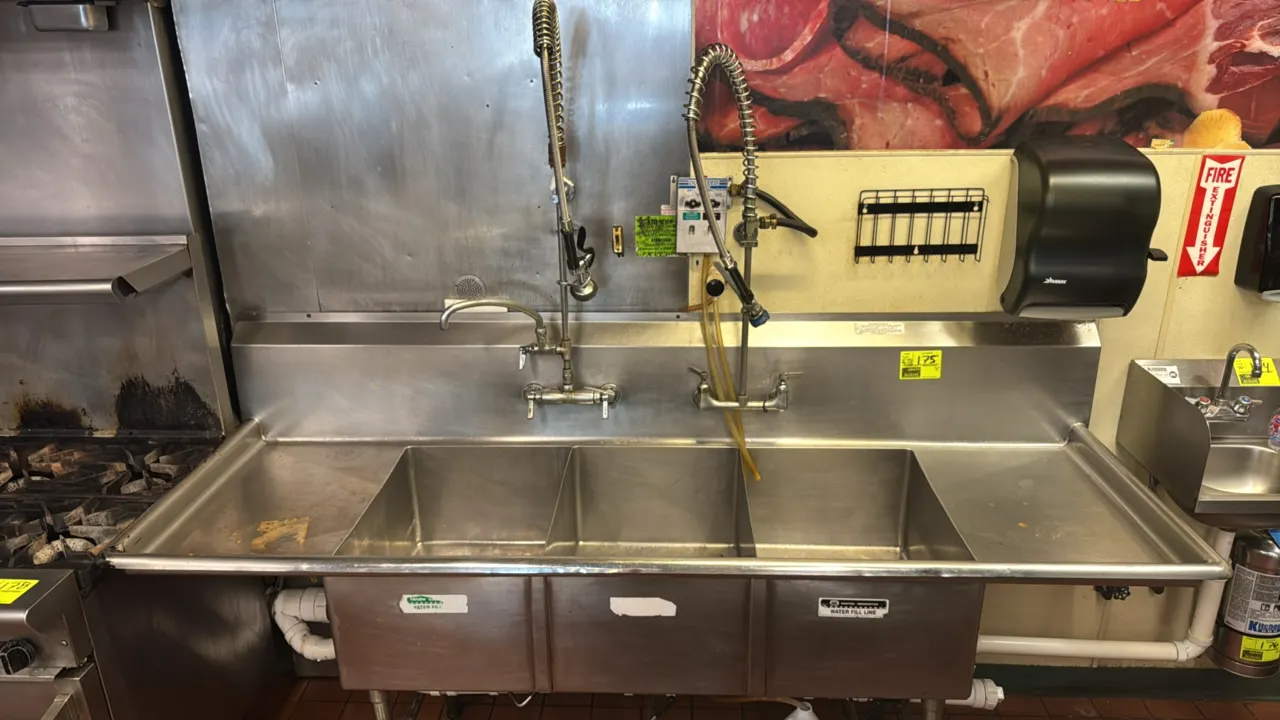 Stainless steel 3-compartment sink. Features left and right drainboards, (2) splash-mount pre-rinse faucet assemblies, and DEMA Duo-Feed chemical disp