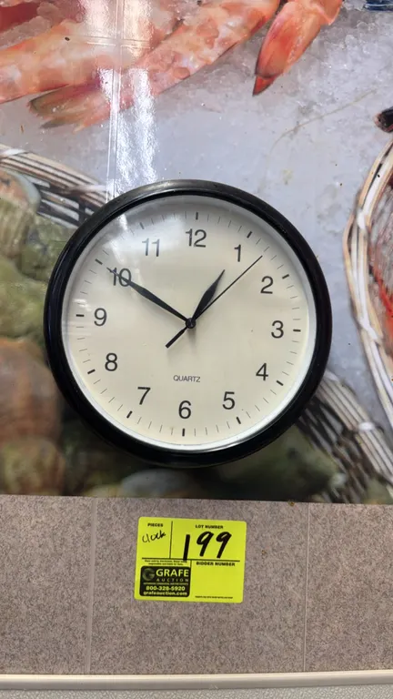 Poly round wall clock. Features a black frame, off-white dial face with Arabic numerals, and quartz movement. 11"Dia. Designed for wall mounting.