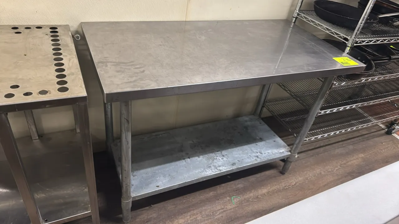 Stainless steel work table. Features a flat top, galvanized lower undershelf, and tubular legs with adjustable bullet feet. Dimensions: 48"L x 24"W.