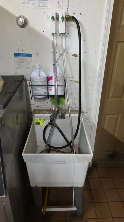 Poly basin sink. Features metal legs, faucet assembly, wall-mounted chemical sanitizer dispensing system, and metal bottle rack. Dimensions: 20" x 24"